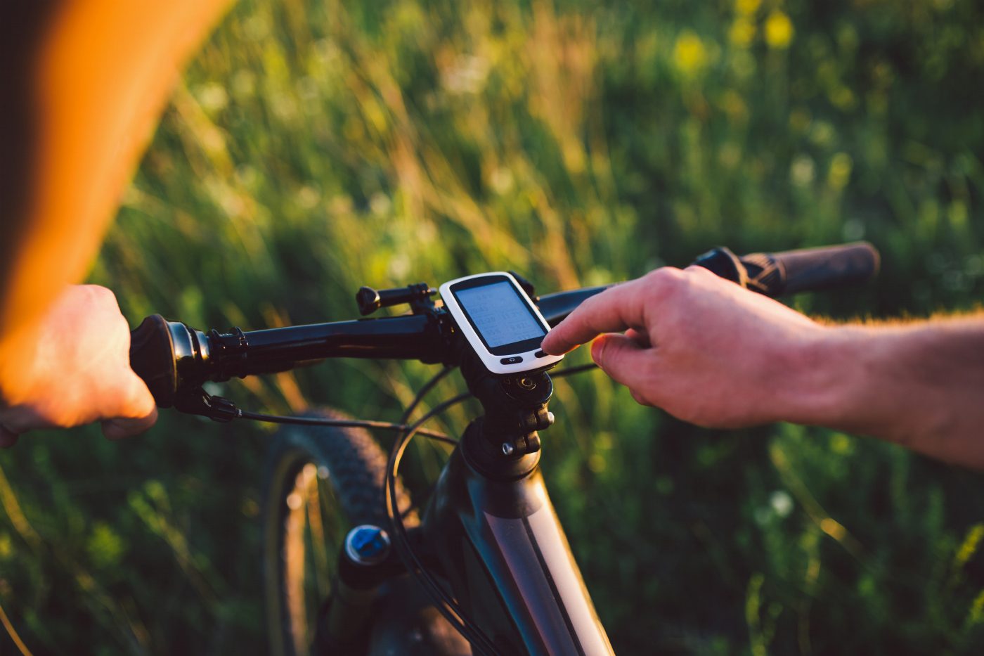 Cyklist trycker på en knapp på en GPS-cykeldator som visar datafält, på ett MTB-styre i kvällsljus
