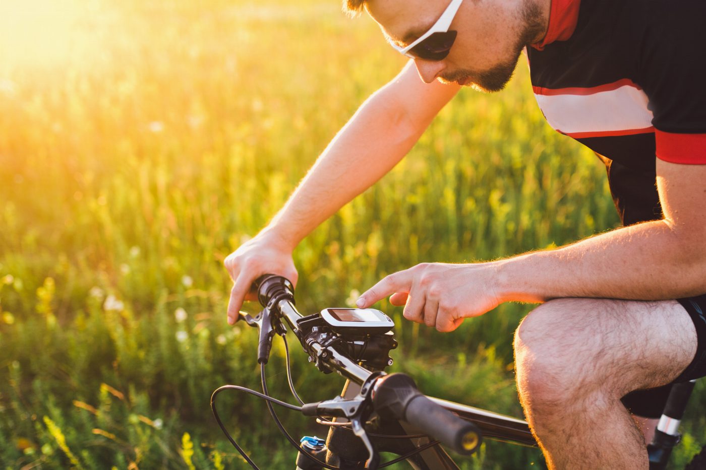 Cyklist böjer sig fram och pekar på en GPS-cykeldator på mountainbike-styret i motljus